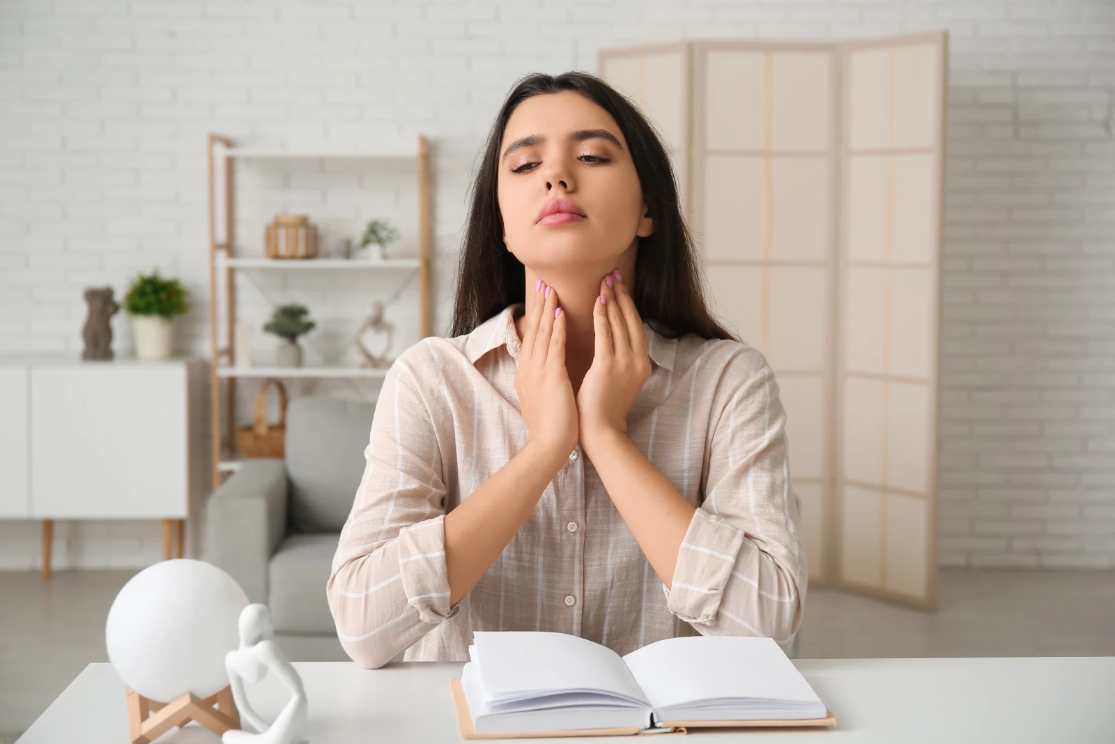 Woman touching her neck and throat while sitting at a desk in a bright home office